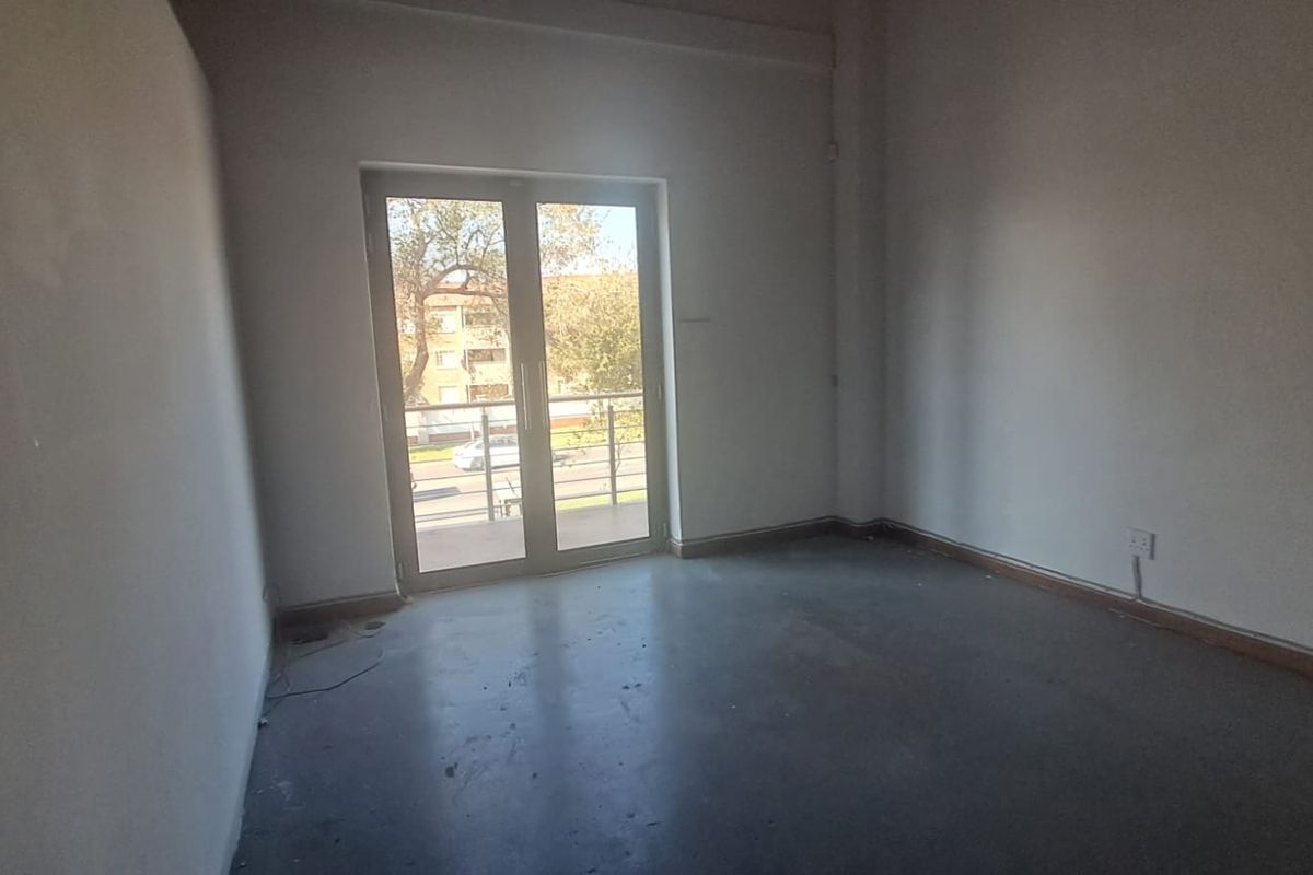 An empty, neutral-toned bedroom featuring a double glass door that provides access to a balcony and allows for natural light.