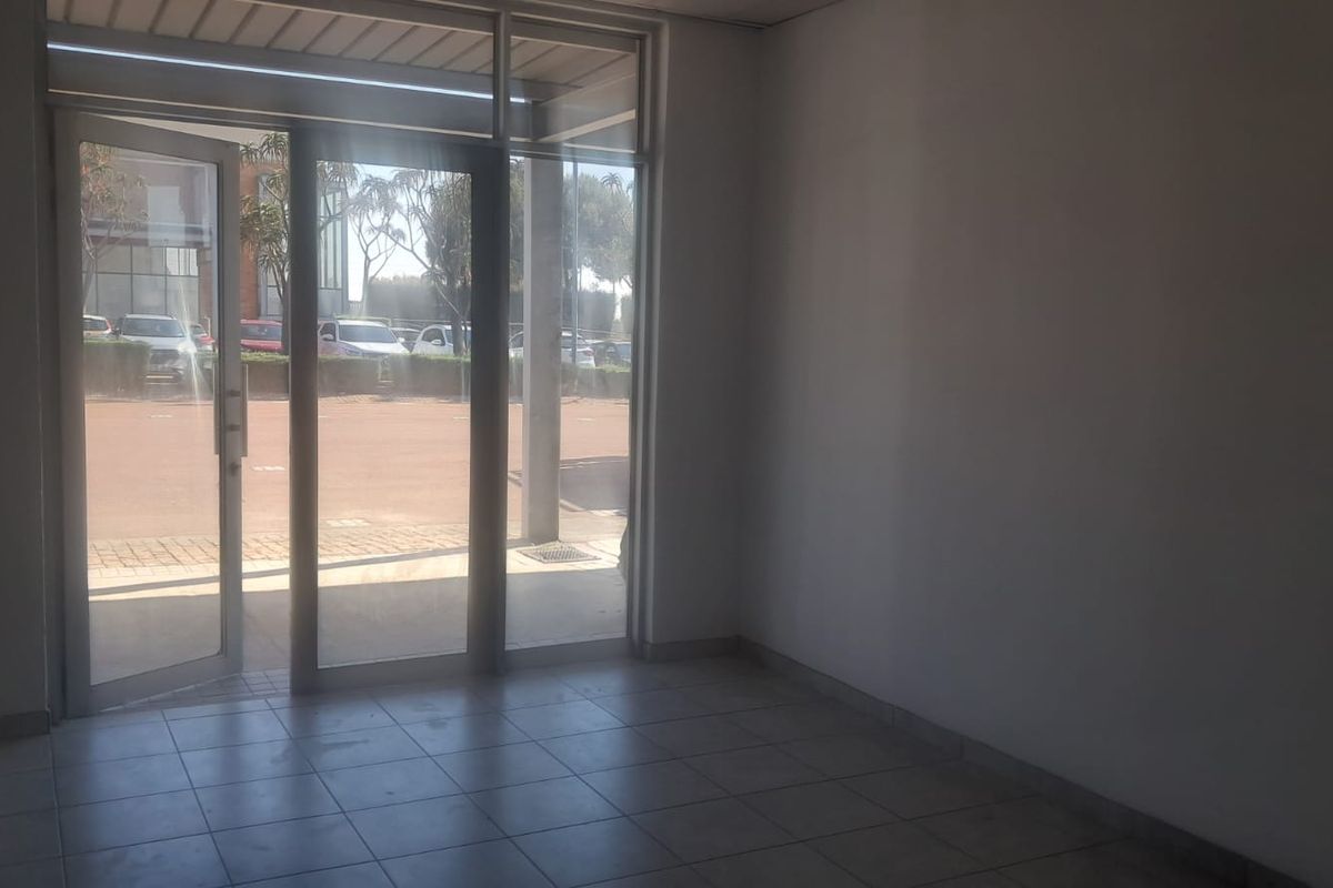 A bright, empty entrance area featuring tiled flooring and large glass doors providing direct access to the exterior parking area.