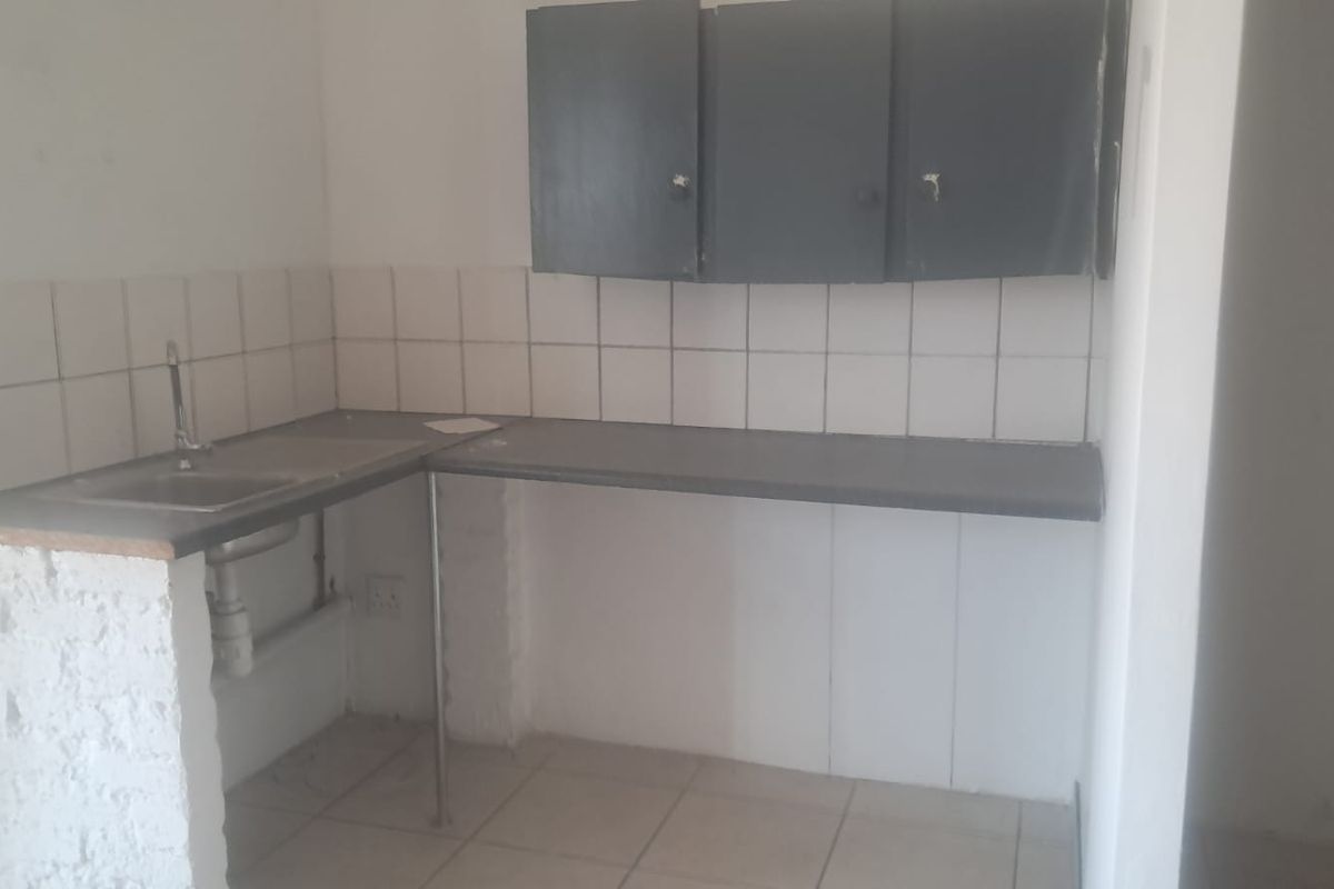 A basic, empty kitchenette featuring a sink, tiled backsplash, laminate countertop, and wall-mounted storage cabinets in a functional industrial space.