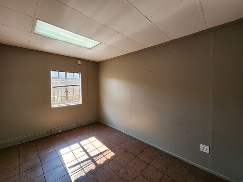 A vacant office space featuring tiled flooring, a suspended ceiling with recessed lighting, and a window with security bars.