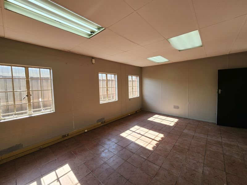 An empty office space featuring tiled flooring, recessed fluorescent lighting, and windows fitted with security bars.