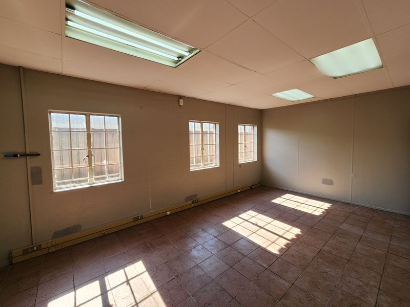 An empty office space featuring tiled flooring, suspended ceilings with fluorescent lighting, and windows fitted with security bars.