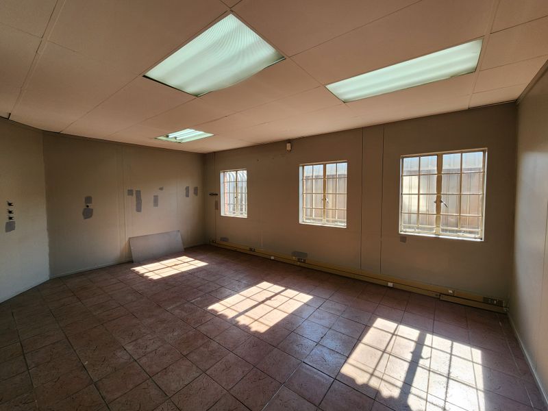An empty office space featuring tiled flooring, recessed fluorescent lighting, and security bars on the windows, requiring minor cosmetic wall repairs.