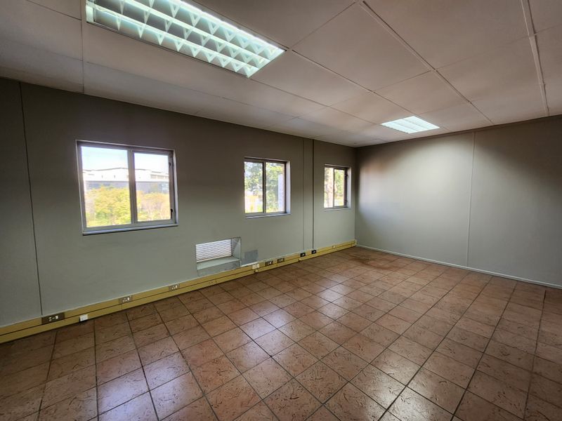 An empty office space featuring tiled flooring, perimeter electrical trunking, and recessed fluorescent lighting within a suspended ceiling.