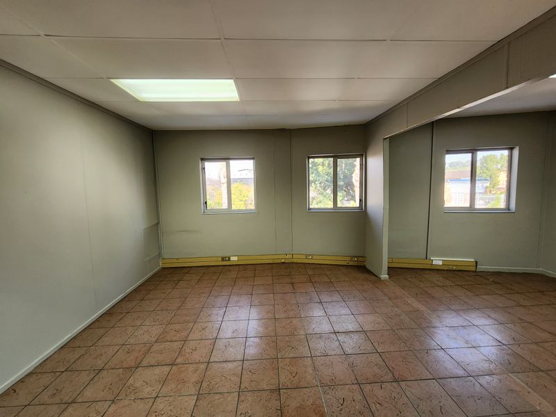 An empty office space featuring ceramic tile flooring, suspended ceiling with recessed lighting, and wall-mounted electrical trunking.