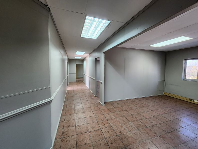 An empty office space featuring tiled flooring, recessed fluorescent lighting, and neutral wall finishes with chair rail molding.