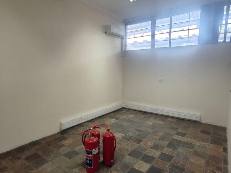 A functional, empty office space featuring tiled flooring, an exposed timber beam, split-system air conditioning, and ample natural light from multi-pane windows.