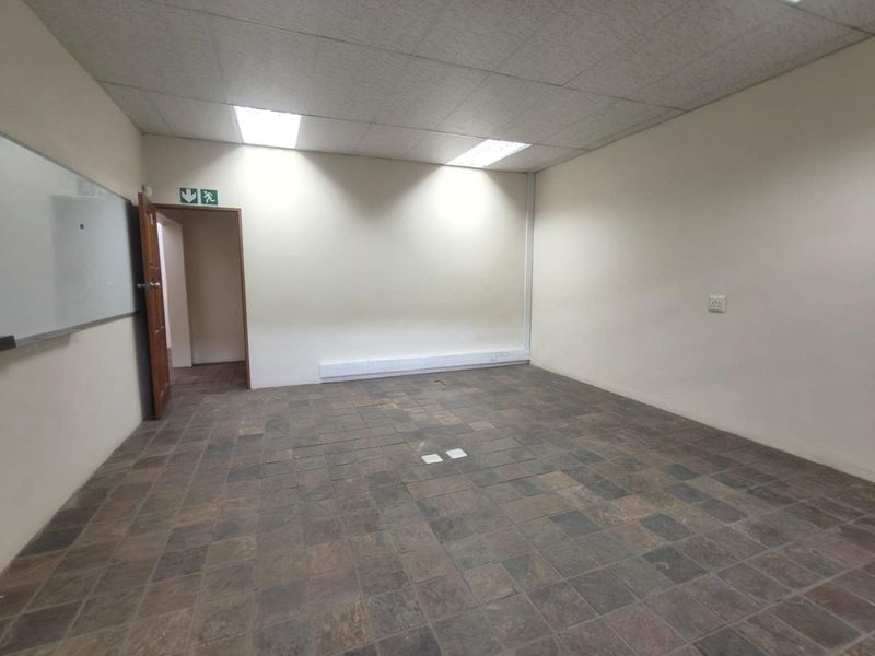 An empty commercial office space featuring slate tile flooring, a suspended ceiling with recessed lighting, and a wall-mounted whiteboard.