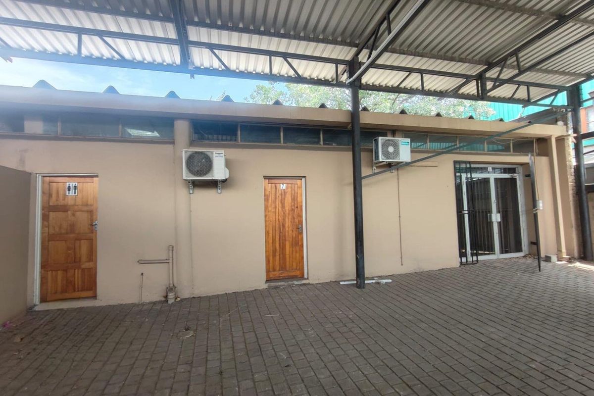 A covered outdoor paved area featuring multiple access doors, wall-mounted air conditioning units, and clerestory windows along the building facade.