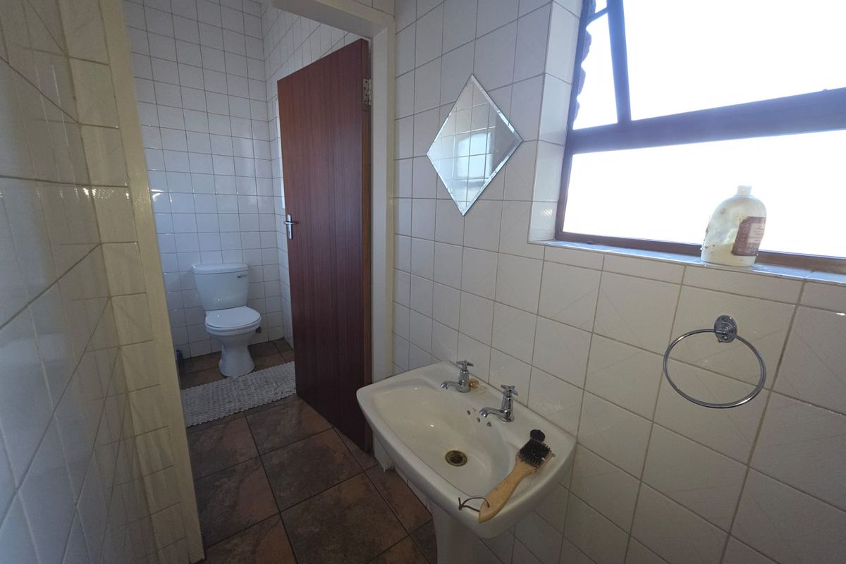 A functional bathroom featuring a pedestal basin, tiled walls, and a separate toilet area with a window for natural light.