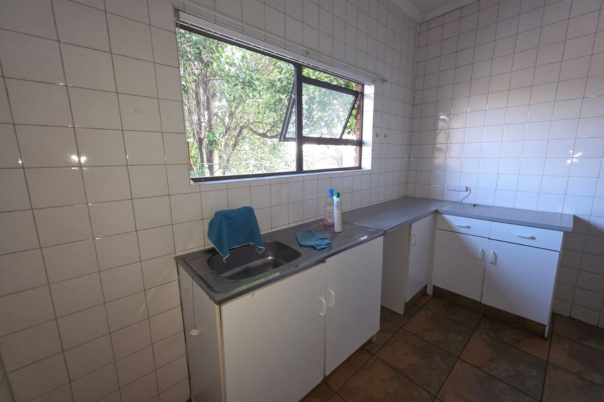 A functional kitchen area featuring tiled walls, a stainless steel sink, built-in cabinetry, and a window overlooking the garden.