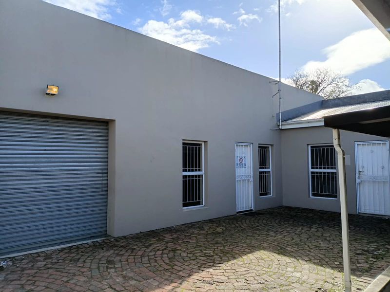 Rear exterior view of the office property featuring a paved courtyard, roller shutter door, and secure access points with security bars.