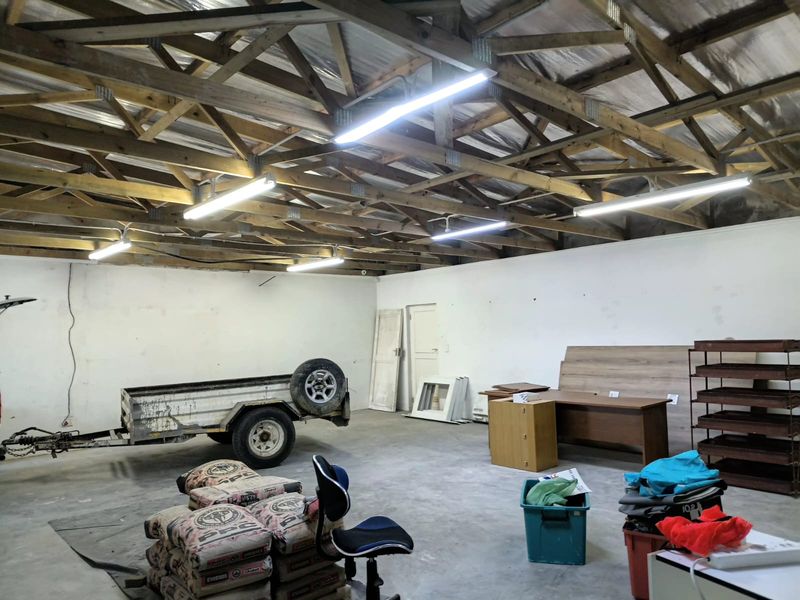 Spacious garage or utility area featuring exposed timber roof trusses, concrete flooring, and functional overhead fluorescent lighting.