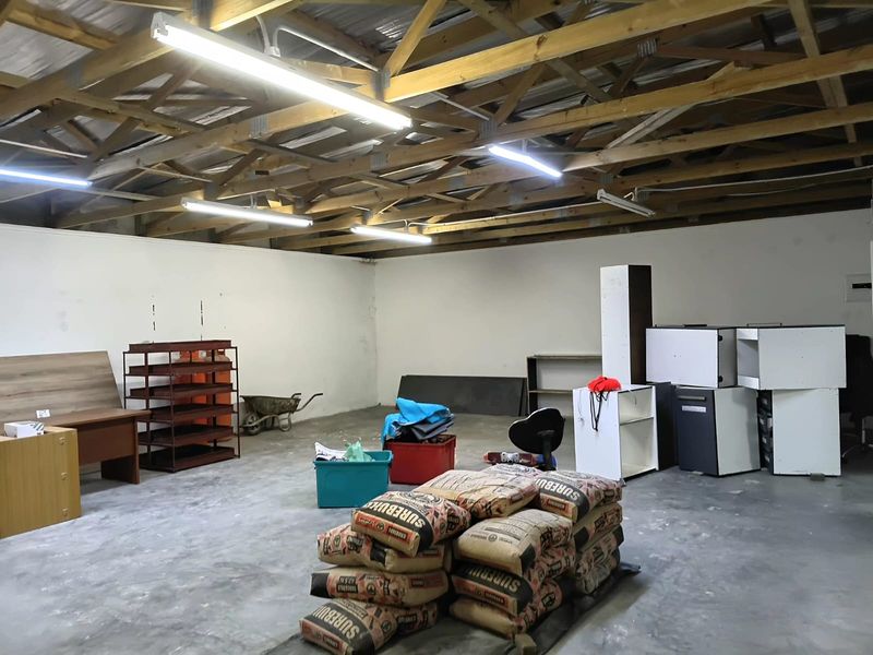 Spacious open-plan office area featuring exposed timber roof trusses, concrete flooring, and functional strip lighting, suitable for a versatile workspace layout.