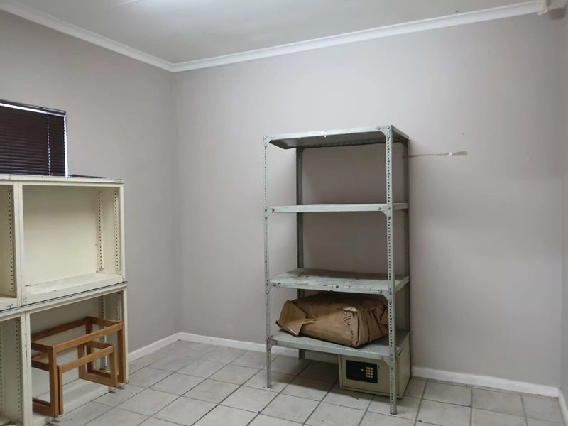 A functional office space featuring tiled flooring, neutral wall finishes, and window blinds, suitable for a professional workspace or storage area.