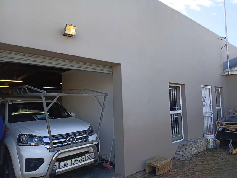 Rear exterior view of the office property featuring a roller shutter garage entrance, security-fitted windows, and paved outdoor area.