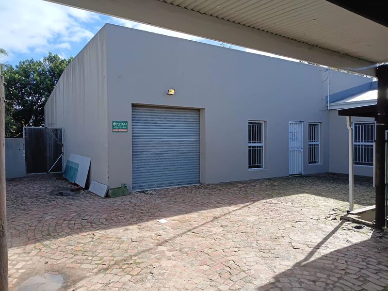 Rear exterior view of the office building featuring a roller shutter door, security-fitted windows, and a paved courtyard area.