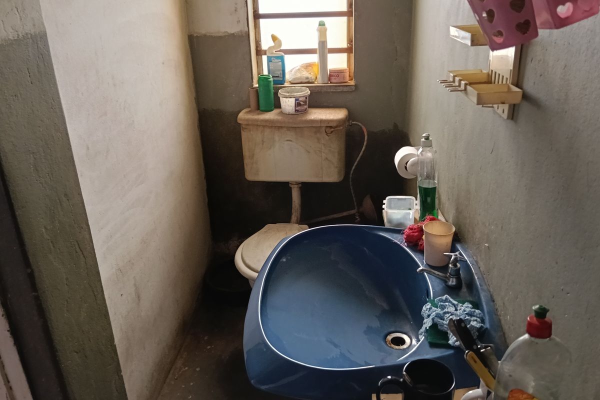 A small, functional bathroom featuring a blue pedestal basin and a standard toilet, requiring cosmetic updates and maintenance to improve the overall finish.
