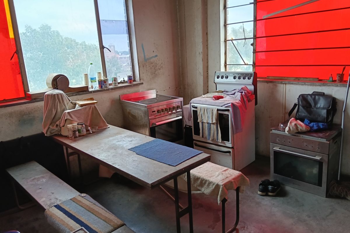 Industrial kitchen space featuring multiple freestanding ovens and large windows with red tinting, requiring significant refurbishment and modernization.