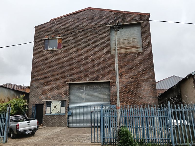 Industrial warehouse building featuring a multi-level brick facade, large roller shutter access doors, and secure perimeter fencing.