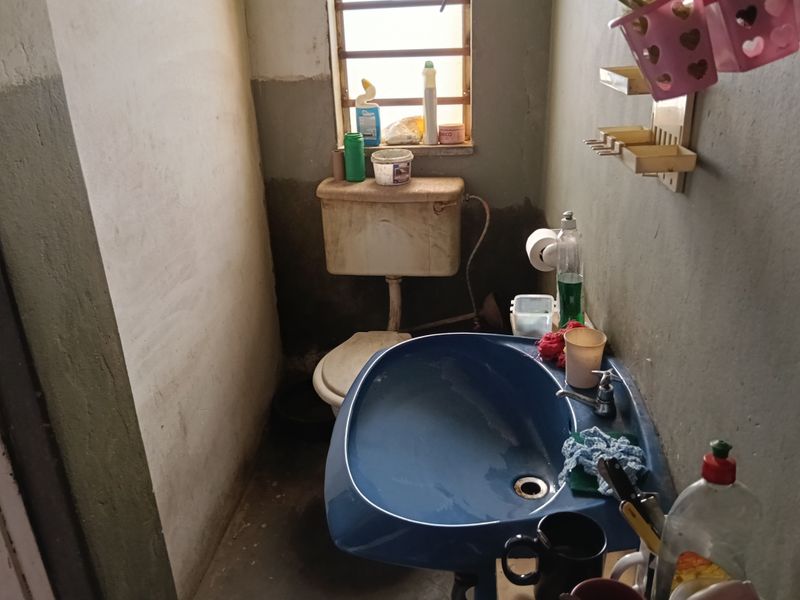 A small, functional bathroom featuring a blue pedestal basin and a standard toilet, requiring cosmetic updates and maintenance to improve the overall finish.