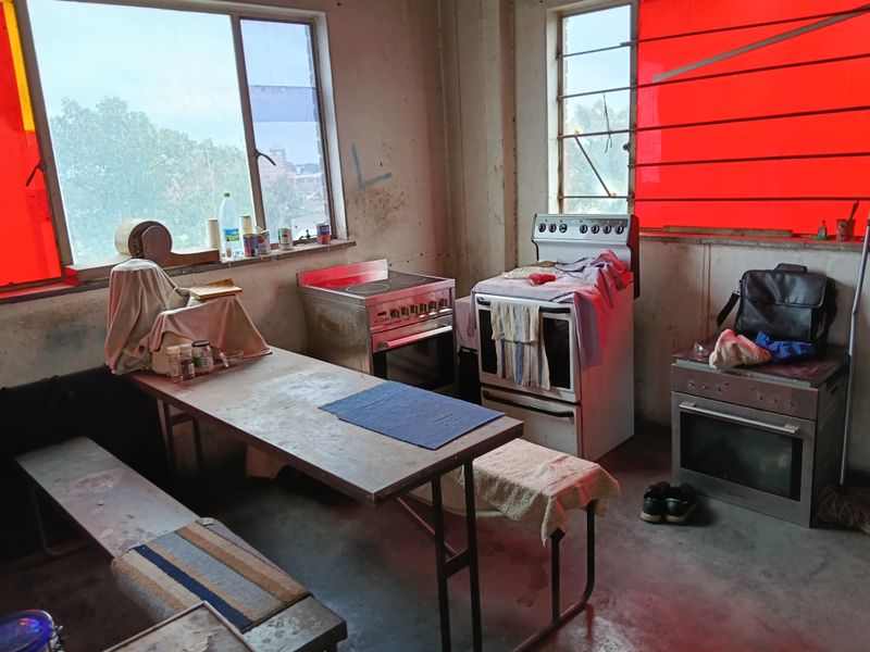 Industrial kitchen space featuring multiple freestanding ovens and large windows with red tinting, requiring significant refurbishment and modernization.