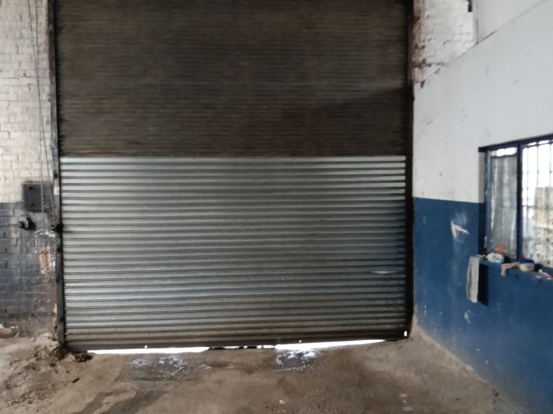 Industrial warehouse space featuring a large metal roller shutter door, exposed brickwork, and concrete flooring.