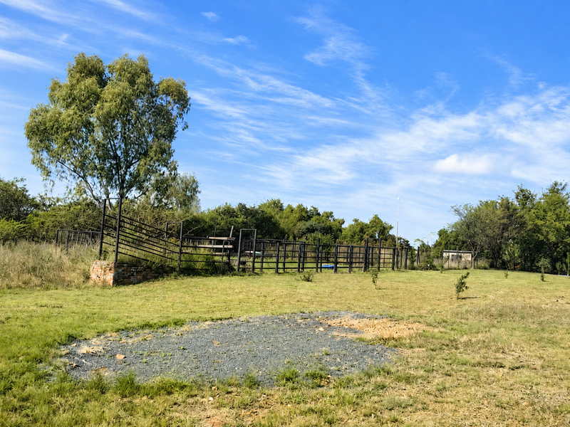 Expansive farm garden area featuring established trees, metal livestock fencing, and a brick retaining wall structure.