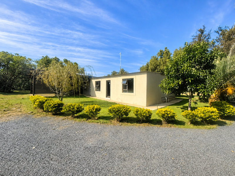 A view of the front exterior of the farm building, featuring a gravel driveway, landscaped garden, and simple facade with casement windows.