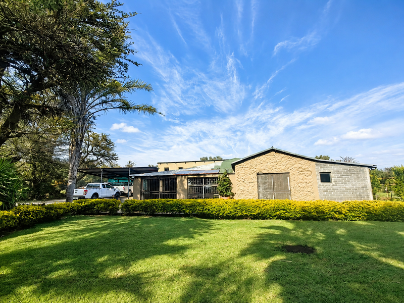 Rear view of the farm property featuring stone and block masonry, a metal roof, and an attached carport set against a well-maintained lawn.
