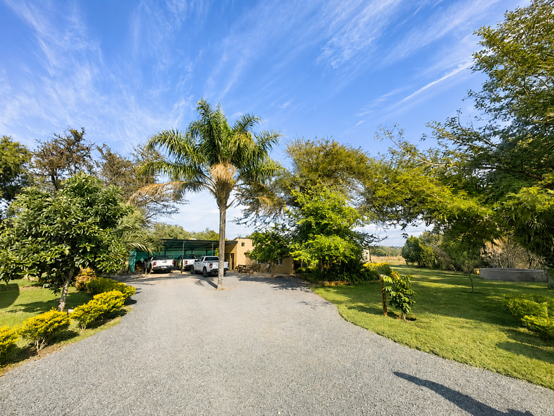 A wide-angle view of a farm property featuring a gravel driveway, mature landscaping, and a functional carport area.