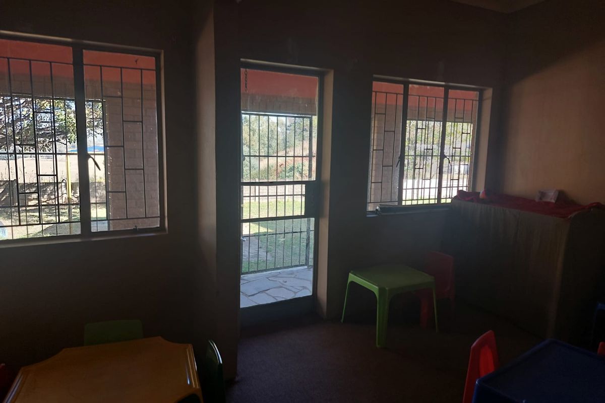 A dimly lit interior space featuring large windows with security bars and a glass-panelled door leading to an outdoor area.