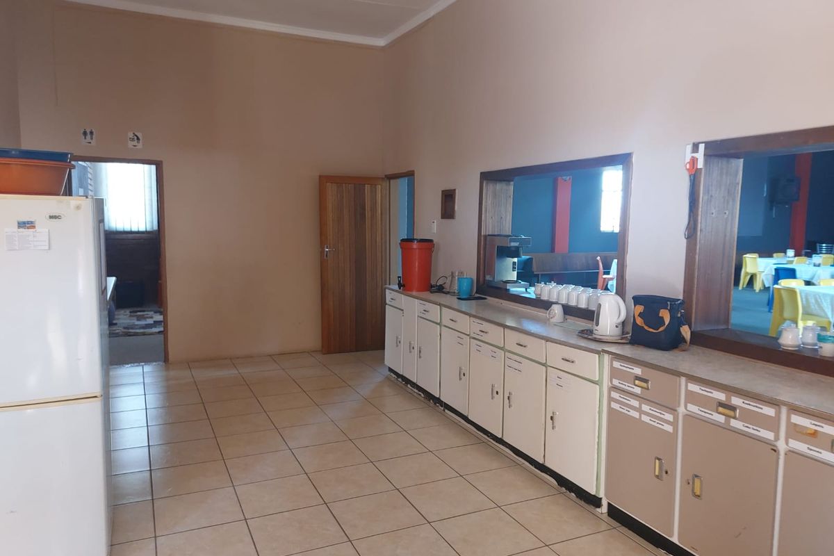 A functional commercial kitchen or service area featuring built-in cabinetry, tiled flooring, and a service window overlooking an adjacent dining space.