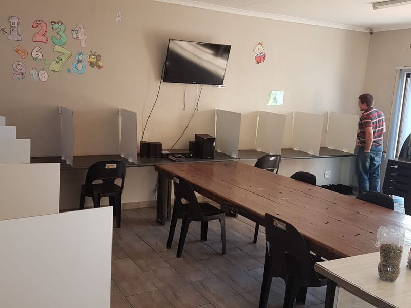 A functional commercial office space featuring built-in desk partitions, tiled flooring, and wall-mounted media equipment, suitable for a collaborative work environment.