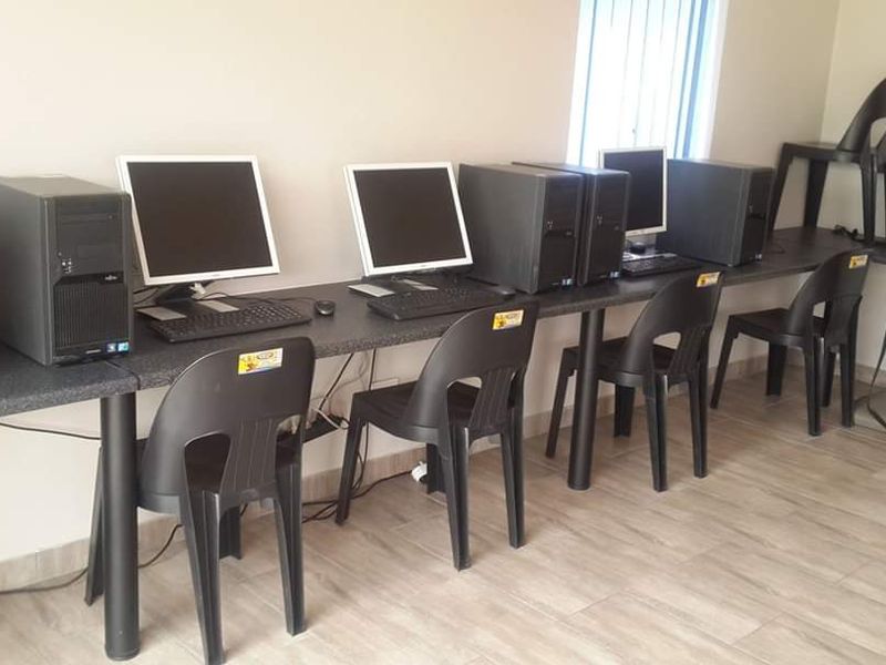A functional office space featuring a long built-in desk, tiled flooring, and vertical window blinds, suitable for a computer workstation area.