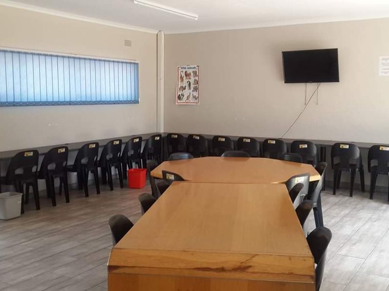 A functional office or meeting space featuring tiled flooring, vertical window blinds, and a wall-mounted television.