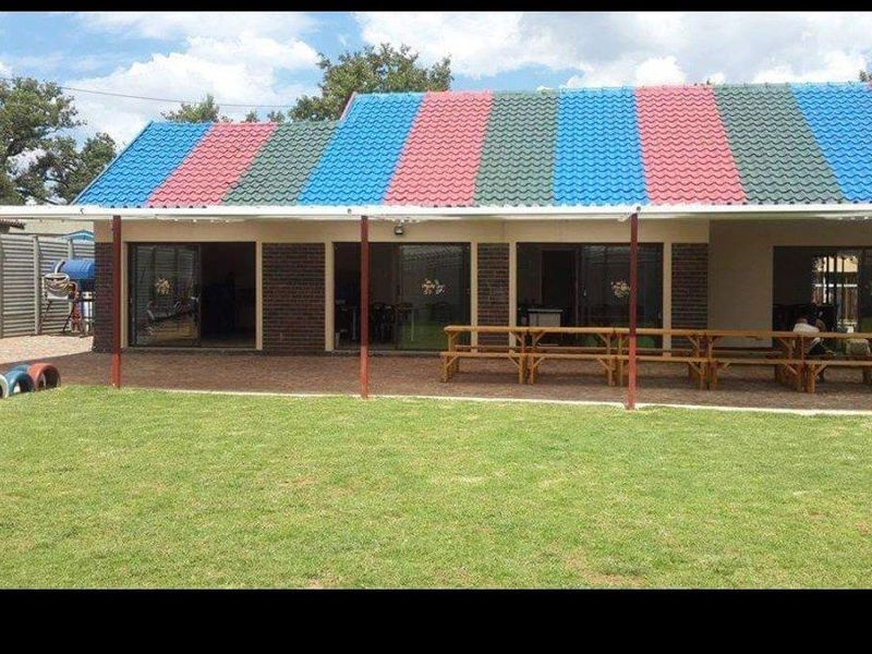 Rear view of a commercial property featuring a covered patio area, paved flooring, and a large lawn, with distinctive multi-colored roof tiling.