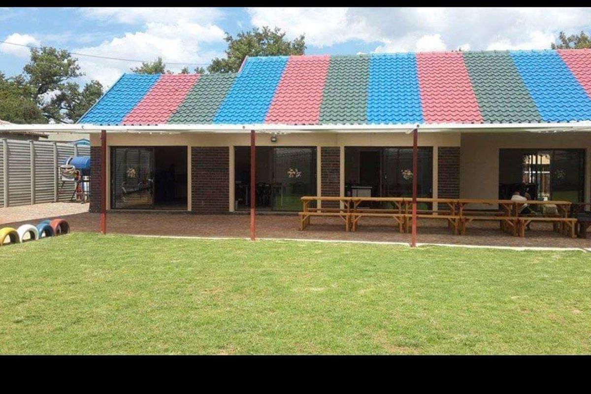 Rear view of a commercial property featuring a covered patio area, paved flooring, and a large lawn, with distinctive multi-colored roof tiling.