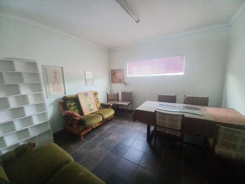 A functional living area featuring tiled flooring, neutral walls, and horizontal window blinds, offering a versatile space for commercial or office use.