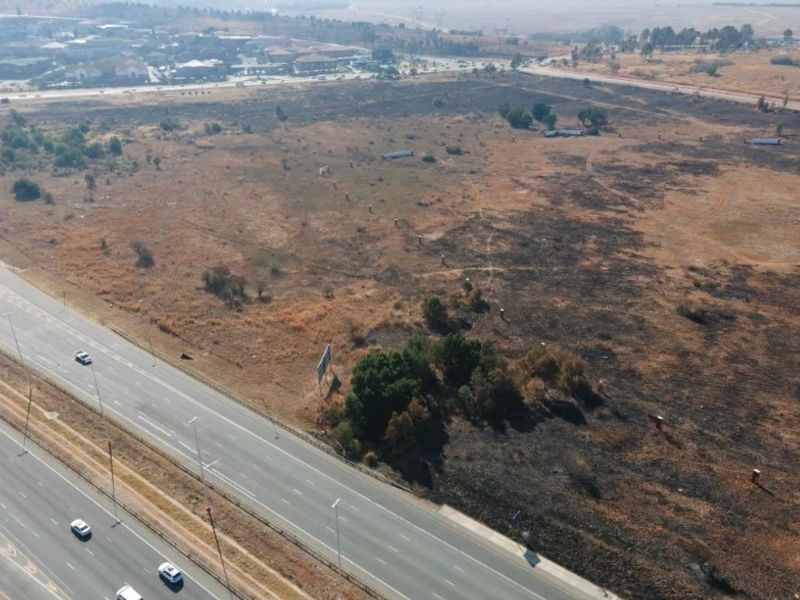 Aerial view of a large, undeveloped industrial land parcel situated adjacent to a major highway, offering significant development potential.