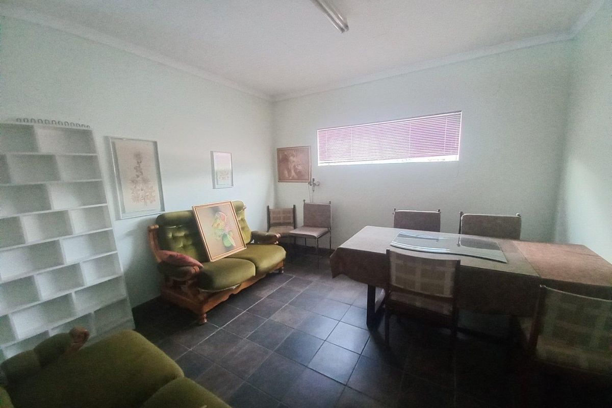 A functional living area featuring tiled flooring, neutral walls, and horizontal window blinds, offering a versatile space for commercial or office use.
