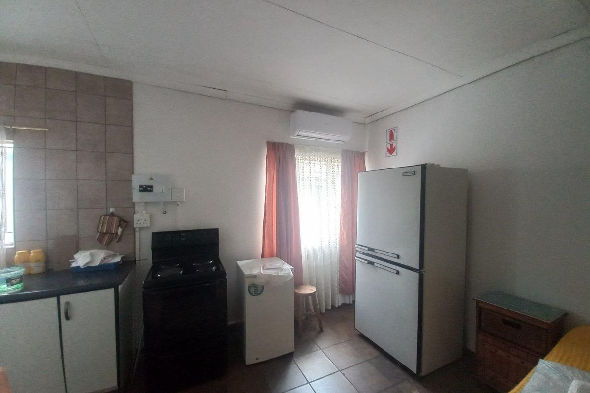 A compact kitchen area featuring tiled flooring, a tiled splashback, and an installed air conditioning unit, showing signs of wear in the ceiling.