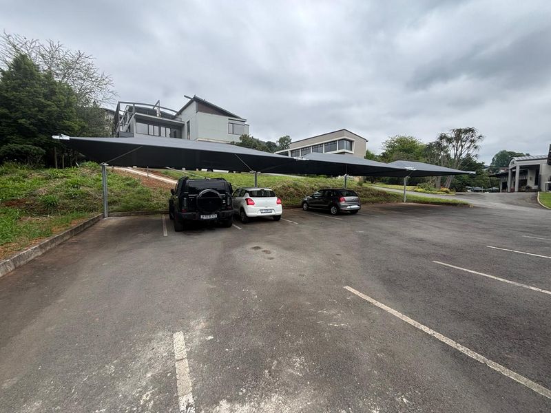 Commercial parking area featuring a large shade cloth carport structure over paved asphalt bays with concrete curbing.