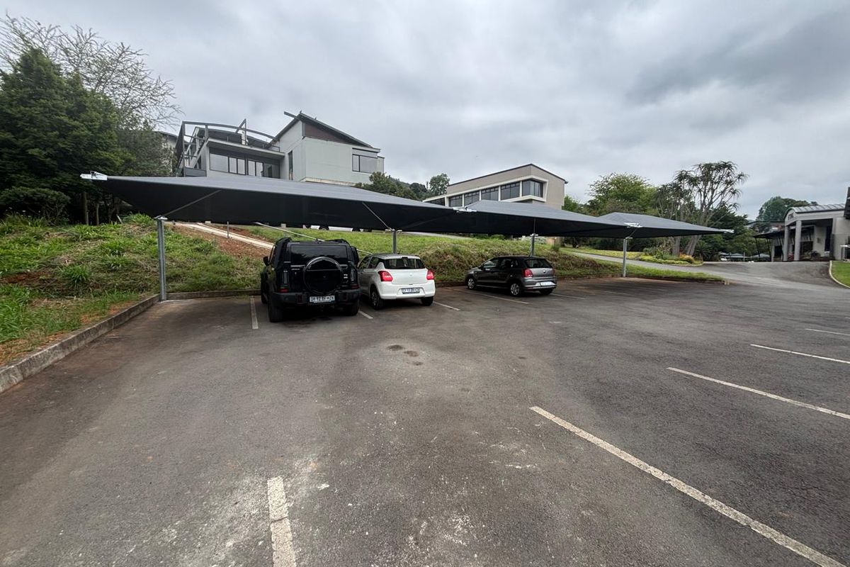 Commercial parking area featuring a large shade cloth carport structure over paved asphalt bays with concrete curbing.