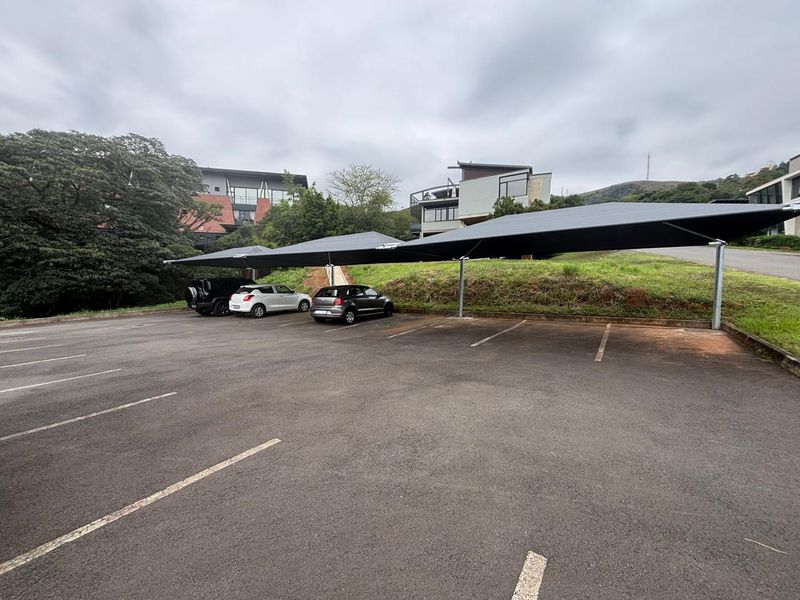 A paved commercial parking area featuring multiple covered parking bays with shade cloth structures.