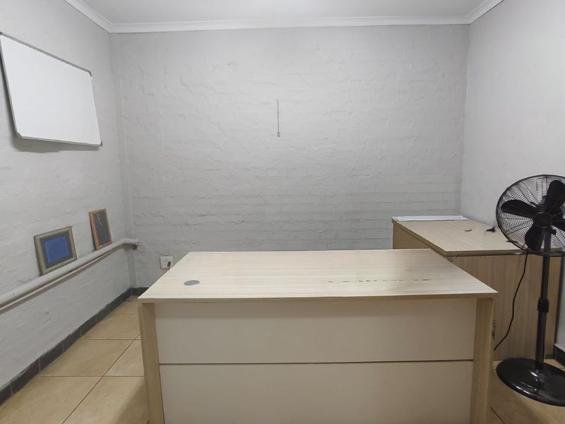 A functional office space featuring ceramic tiled flooring, exposed brick walls, and overhead fluorescent lighting, suitable for a professional work environment.