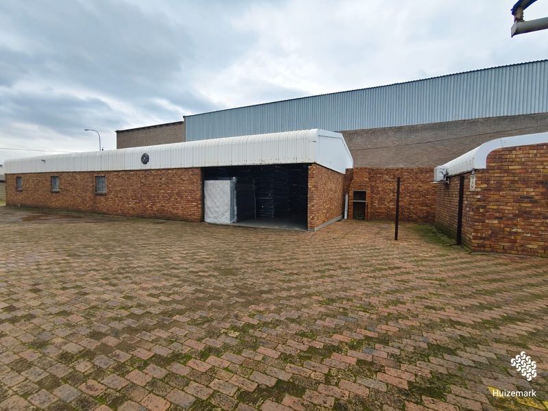 Rear exterior view of a commercial property featuring face brick walls, a corrugated metal roof, and a paved courtyard area with a built-in braai.