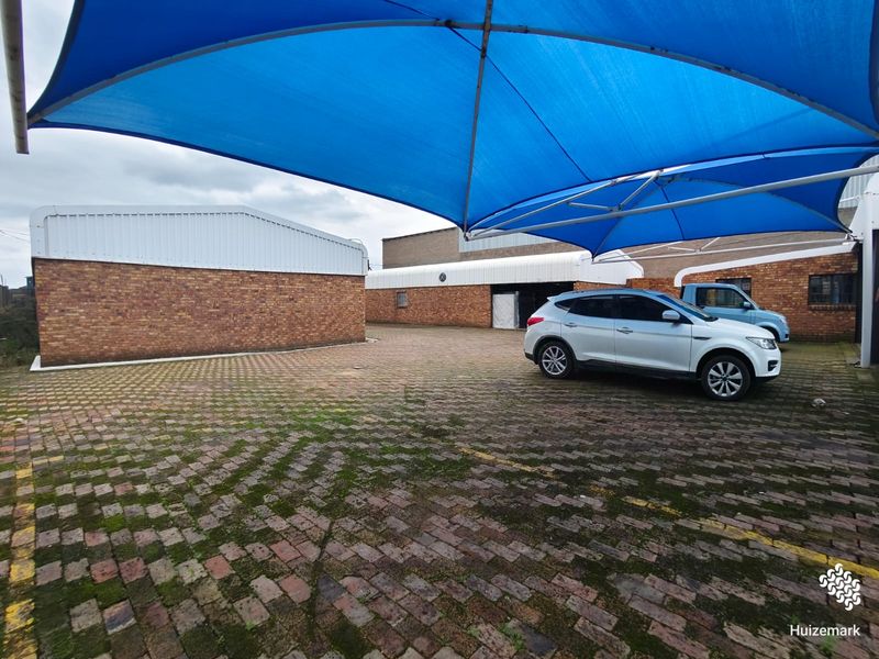 Commercial exterior rear area featuring a paved parking space covered by a large blue shade sail and brick building structures.