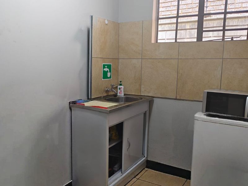 A functional scullery or utility area featuring a stainless steel sink, tiled splashback, and durable tiled flooring.