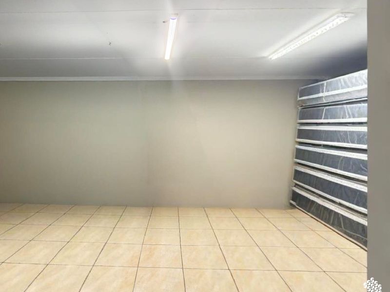 A clean, empty utility space featuring neutral tiled flooring and functional overhead fluorescent strip lighting, suitable for storage or workspace use.